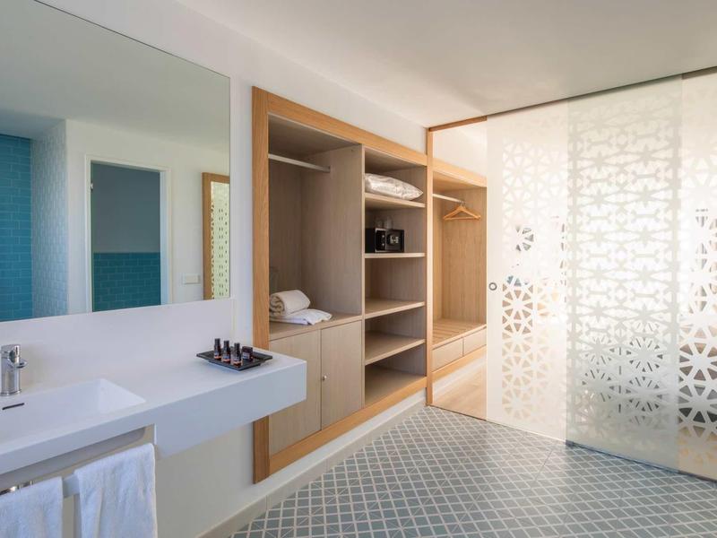 Bright hotel bathroom with modern white sinks and decorative glass walls.