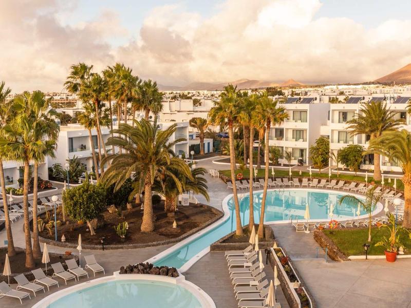 Hotel complex with multiple pools, palm trees, and lounge chairs under cloudy skies.