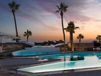 Moderner Swimmingpool mit Palmen am Strand bei Sonnenuntergang