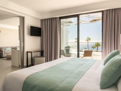 Helles Hotelzimmer mit Doppelbett, grünem Bettüberwurf, Balkon und Meerblick bei Tageslicht.