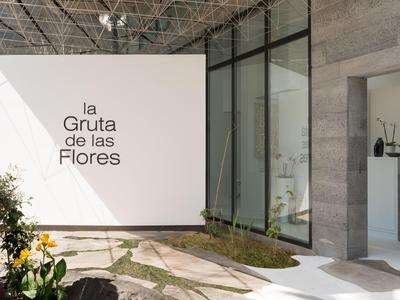 Moderner Eingangsbereich mit weißer Wand und Pflanzen, beschriftet mit La Gruta de las Flores.