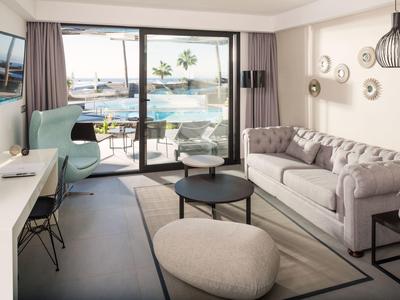 Modern eingerichtetes Wohnzimmer mit grauem Sofa, Sesseln, runden Tischen und großer Glasfront zum Meer.