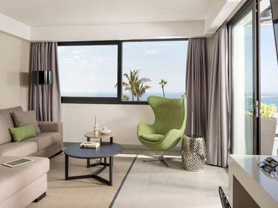 Helles Wohnzimmer mit grauer Couch, grünem Sessel, großem Fenster und modernem Couchtisch.