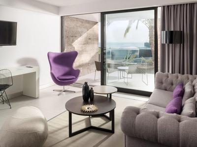 Modernes Wohnzimmer mit lila Sessel, grauem Sofa, Glasfenster und Meerblick.