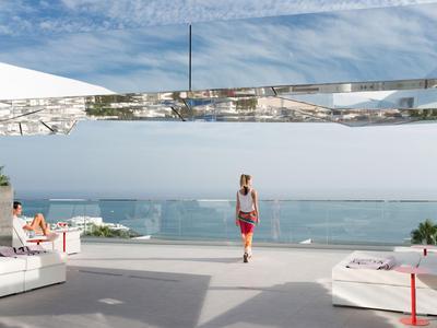 Frau steht auf einer Terrasse mit Blick auf das Meer und entspannte Sitzbereiche bei klarem Himmel.