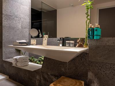 Moderner Waschbeckenbereich mit großem Spiegel, grauen Steinwänden und hängendem Blumendeko.