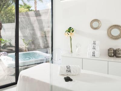 Modernes Behandlungzimmer mit Massagebank, weißer Wand, Dekoration und Blick auf Whirlpool draußen.