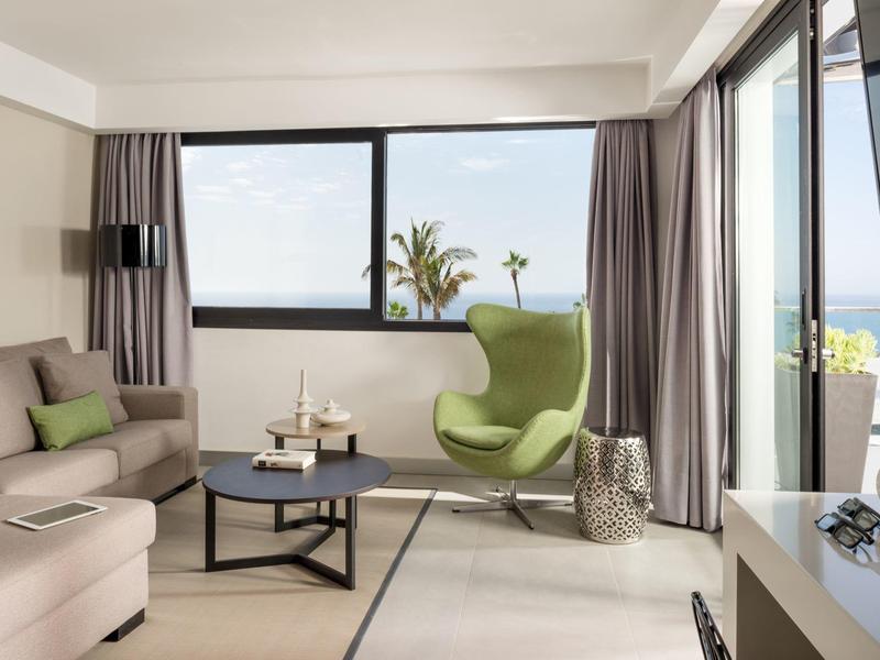 Helles Wohnzimmer mit grauer Couch, grünem Sessel, großem Fenster und modernem Couchtisch.