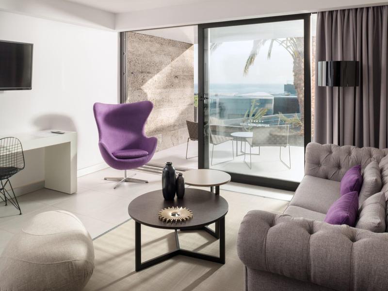 Modernes Wohnzimmer mit lila Sessel, grauem Sofa, Glasfenster und Meerblick.