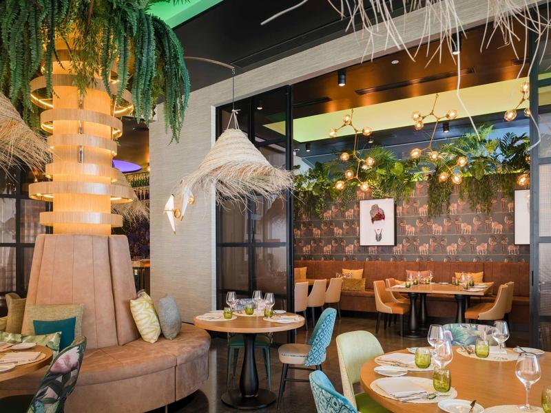 Modernes Restaurant mit Holztischen, bunten Stühlen, hängender Dekoration und gemütlicher Beleuchtung.