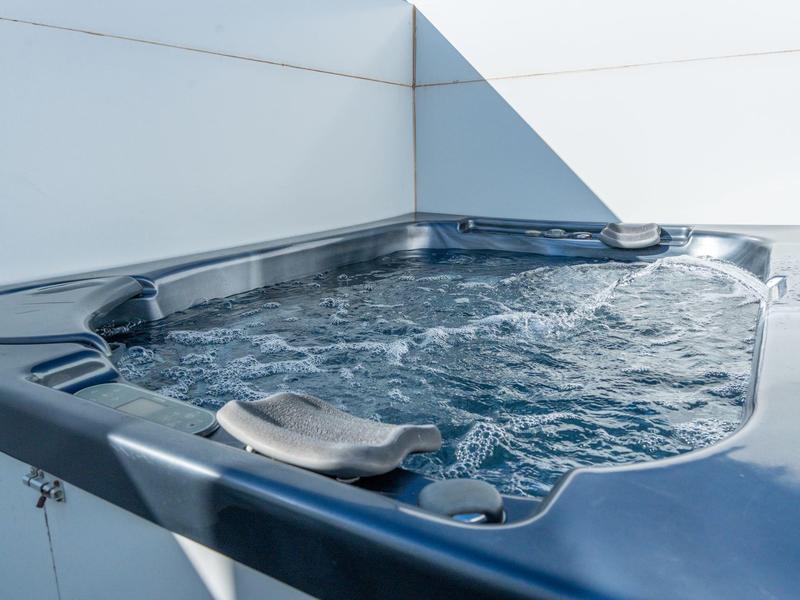 Moderner Whirlpool mit sprudelndem Wasser auf einer weißen Terrasse unter blauem Himmel.