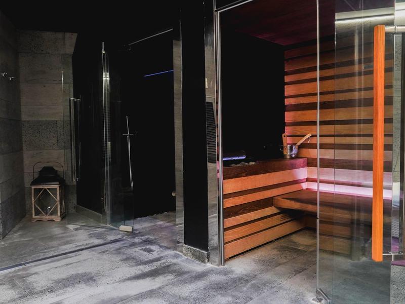 Moderner Wellnessbereich mit Glas-Sauna, Holzbänken und Betonboden in dunklem Ambiente.