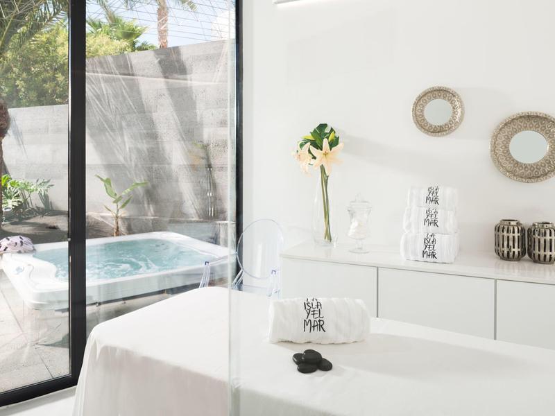 Modernes Behandlungzimmer mit Massagebank, weißer Wand, Dekoration und Blick auf Whirlpool draußen.