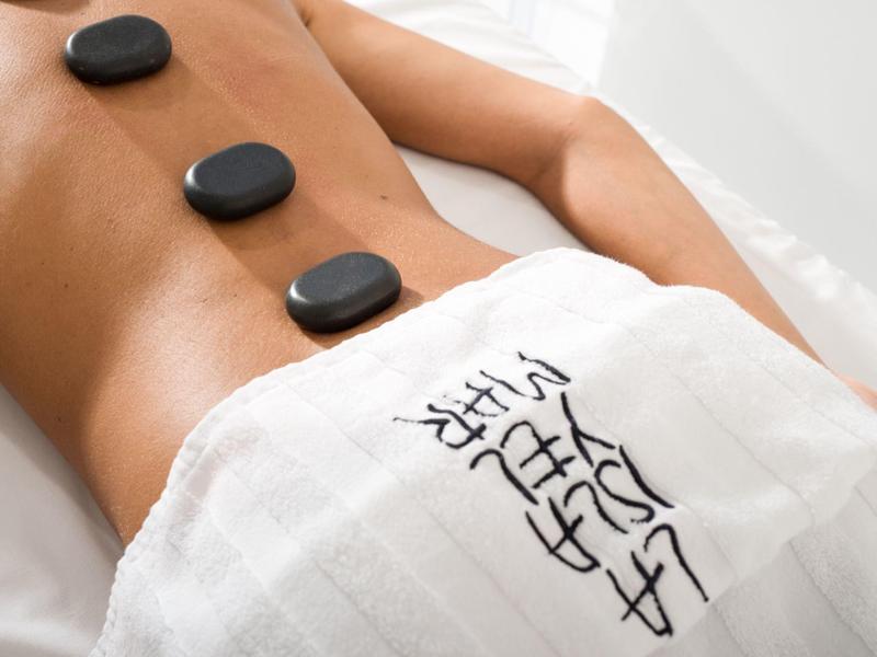 Person liegt mit nacktem Rücken, auf dem vier schwarze Steine zur Hot-Stone-Massage liegen.