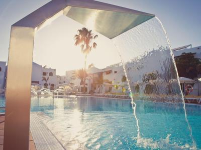 Moderner Pool mit Wasserfall und Blick auf Sonnenuntergang und Palmen im Hotelresort.