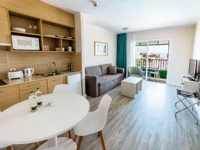 Sala moderna de hotel con mesa blanca, sillones, sofá gris y ventana con vista exterior.