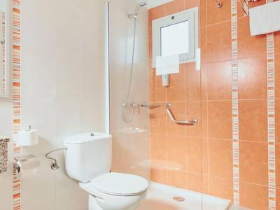 Modern wit-oranje badkamer met toilet, douche en klein raam.