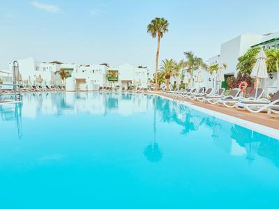 Gran piscina de hotel con tumbonas y palmeras bajo una luz diurna brillante.