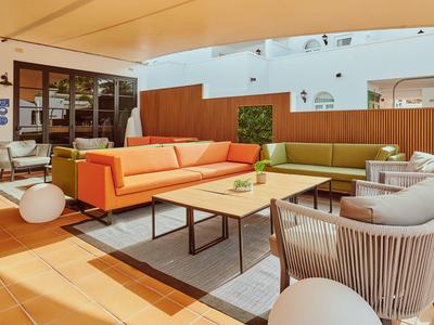 Helle Lounge mit oranger Couch, beigen Sesseln und Holztischen in modernem Hotelinterieur.