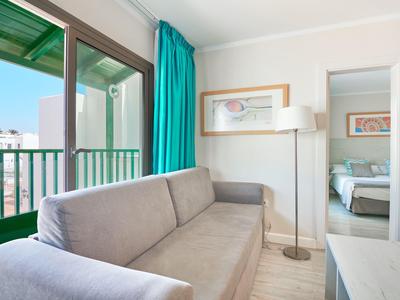 Lichte woonkamer met grijze bank, groen gordijn en uitzicht op balkon en slaapkamer.