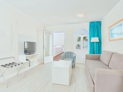 Helles Hotelzimmer mit Sofa, Fernseher und Zugang zu einem Balkon mit Meerblick.