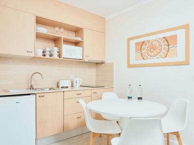 Kleine kitchenette met moderne lichte houten kasten, gootsteen en kleine koelkast.