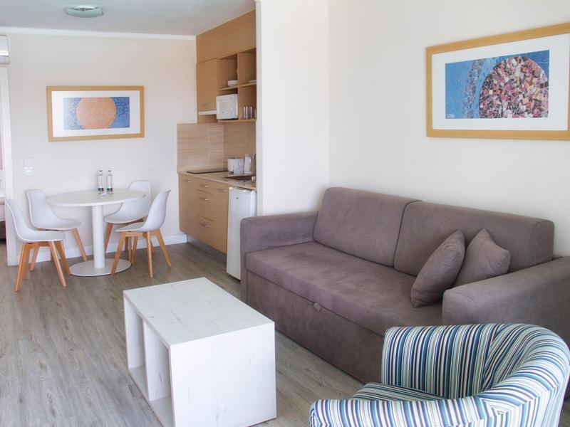 Área de estar moderna con sofá gris, sillón a rayas y pequeño comedor en espacio luminoso.