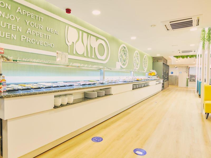 Buffet moderno y luminoso en un hotel con una larga barra y señalización clara en la pared.