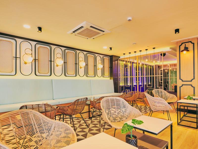 Área de salón de hotel decorada modernamente con sillas de mimbre e iluminación elegante.