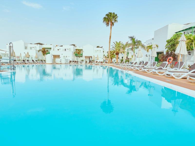 Gran piscina de hotel con tumbonas y palmeras bajo una luz diurna brillante.
