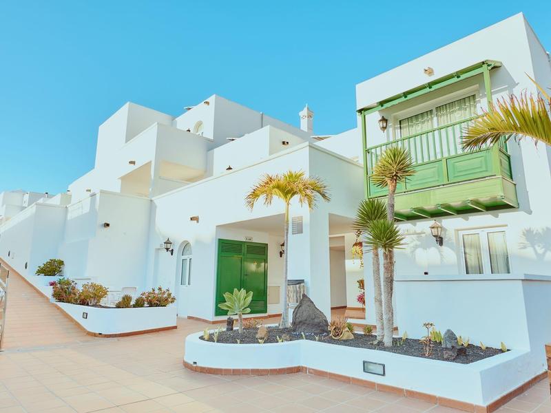 Edificio de hotel blanco con acentos verdes, palmeras y cielo azul claro en destino vacacional.