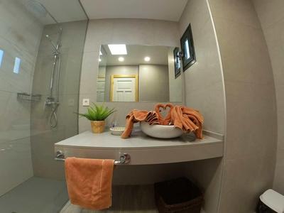 Modernes Badezimmer mit weißer Dusche, großem Spiegel, Waschbecken und orangefarbenen Handtüchern.