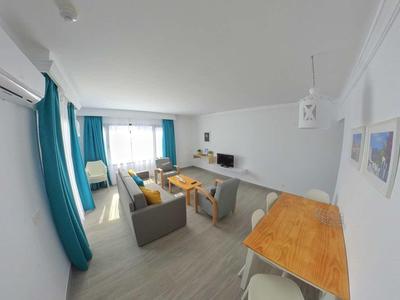 Hell eingerichtetes Wohnzimmer mit grauem Sofa, Holz-Esstisch, blauen Vorhängen und Klimaanlage.