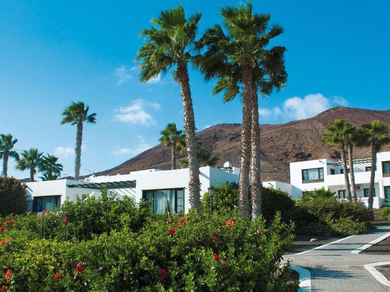 Hotel complex with white buildings, palm trees, and a bright blue sky in the background.