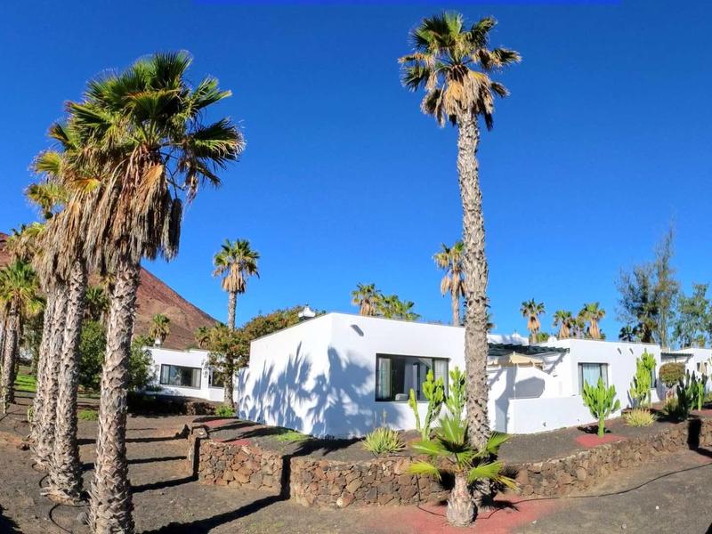 White building in tropical setting with palm trees and blue sky.