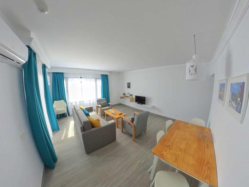 Modern living room with sofa, table, kitchenette, blue-green curtains, white walls.