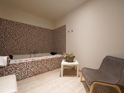 Modernes Badezimmer mit Mosaikfliesen um Badewanne, grauem Sessel und kleinem weißen Tisch.