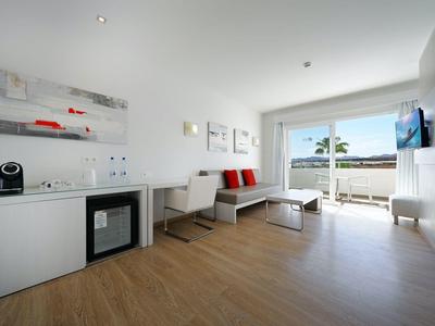 Moderner, heller Wohnraum mit Sofa, Küchenzeile und Meerblick durch große Fenster.