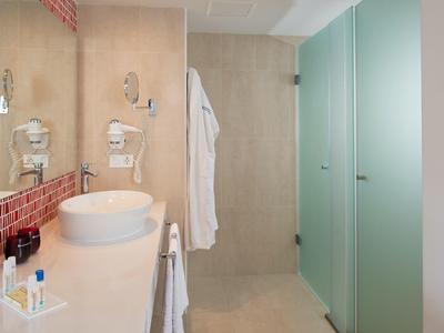 Modernes Badezimmer mit Waschbecken, großem Spiegel, Duschbereich und mattgrünen Glastüren.