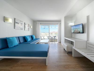 Helles Hotelzimmer mit blauen Sofas und Balkon mit Meerblick.