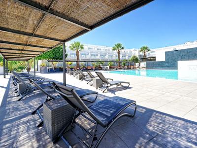 Moderner Poolbereich mit Liegestühlen und schattigem Pergola-Dach am sonnigen Tag.
