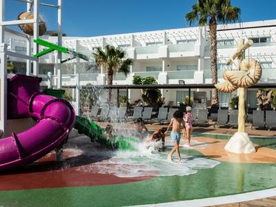 Kinder spielen auf dem spritzenden Wasserspielplatz mit bunten Rutschen unter blauem Himmel.
