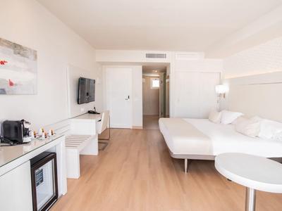 Helles Hotelzimmer mit Doppelbett, Fernseher, Mini-Kühlschrank und Kaffeemaschine, hellem Holzboden.