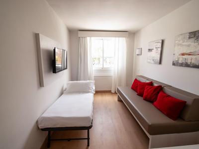 Kleiner Raum mit zwei Sofabetten, weißen Wänden, Holzfußboden und Fenster mit weißen Vorhängen.