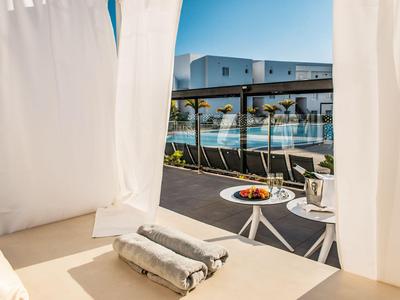 Gemütliche Sonnenterrasse mit weißen Vorhängen, Handtüchern und Blick auf einen Poolbereich.