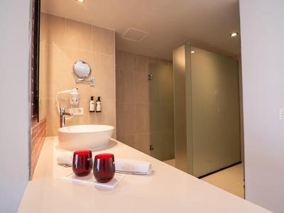 Modernes Badezimmer mit rundem Waschbecken, roten Kerzen und gläsernen Duschabtrennungen.