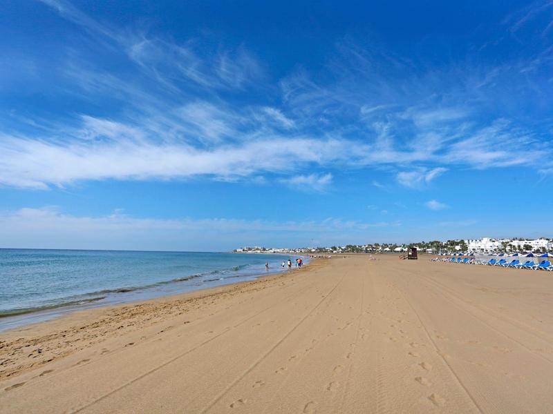 Weiter Sandstrand mit blauem Himmel und ruhiger See am Urlaubsort.