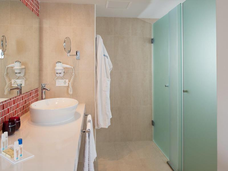 Modernes Badezimmer mit Waschbecken, großem Spiegel, Duschbereich und mattgrünen Glastüren.