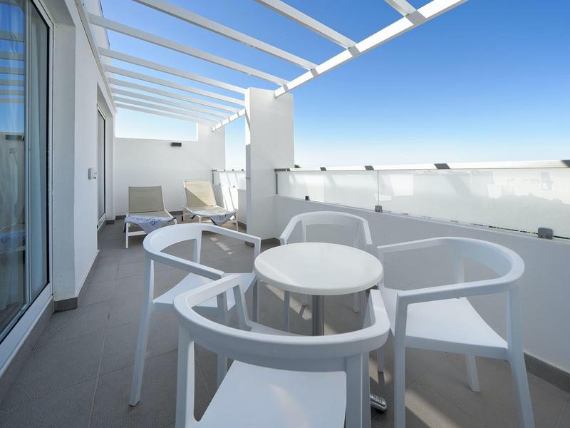 Moderner Balkon mit weißem Möbelset und Glasgeländer mit Meerblick unter blauem Himmel.