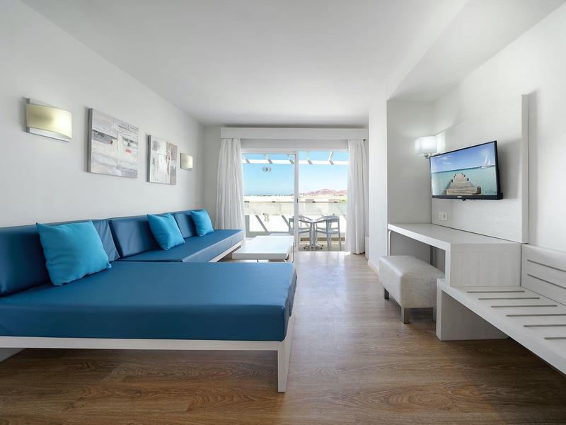 Helles Hotelzimmer mit blauen Sofas und Balkon mit Meerblick.